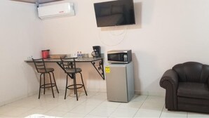 Una pequeña kitchenette equipada con microondas, cafetera y refrigerador. Hay dos sillas y un sofá.