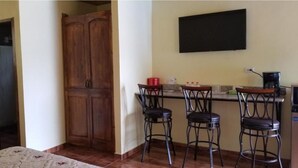 Una cocina con un armario de madera, un televisor montado en la pared y tres taburetes de bar.
