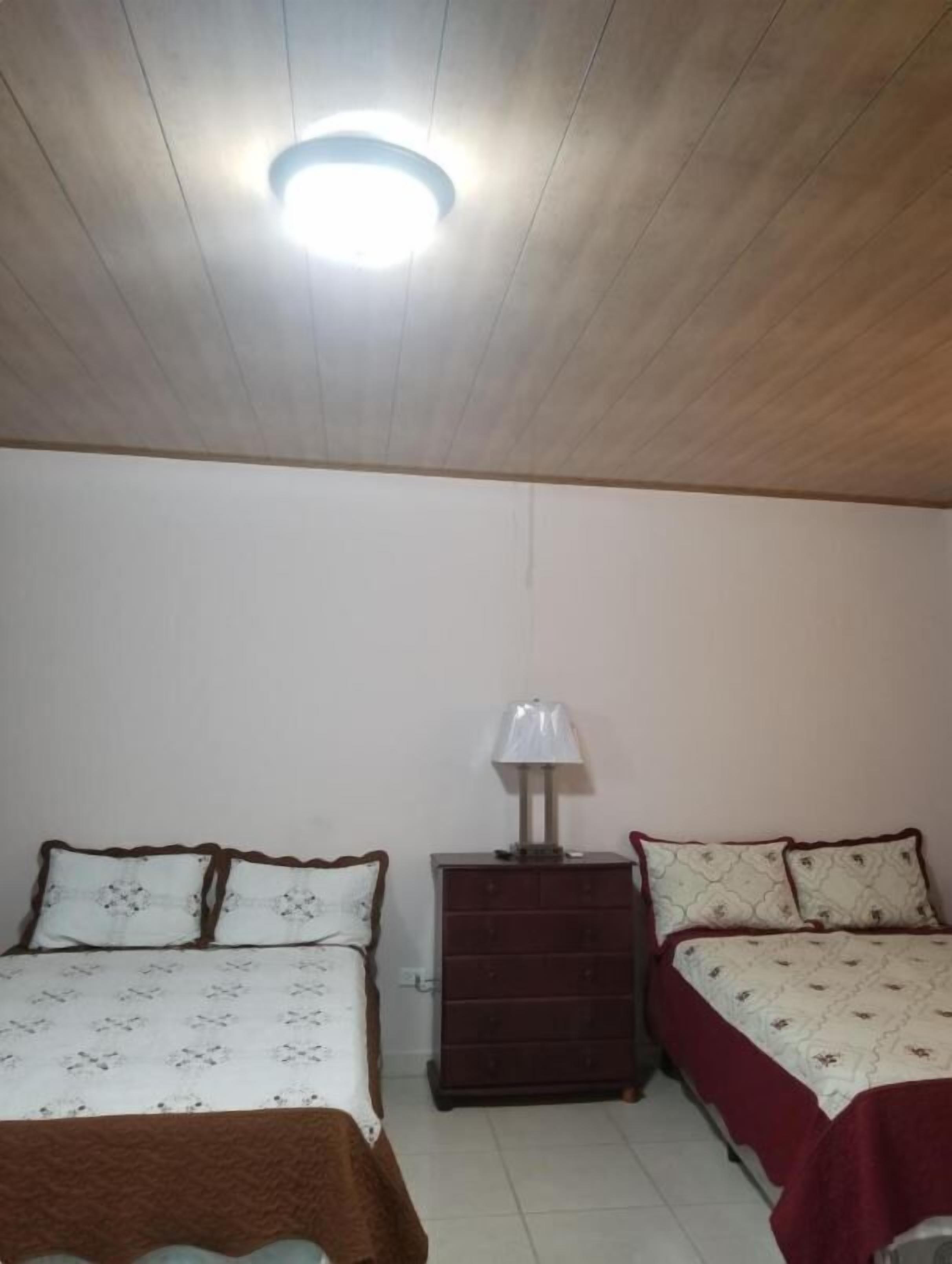 Una habitación con dos camas, un aparador y una lámpara en el techo.
