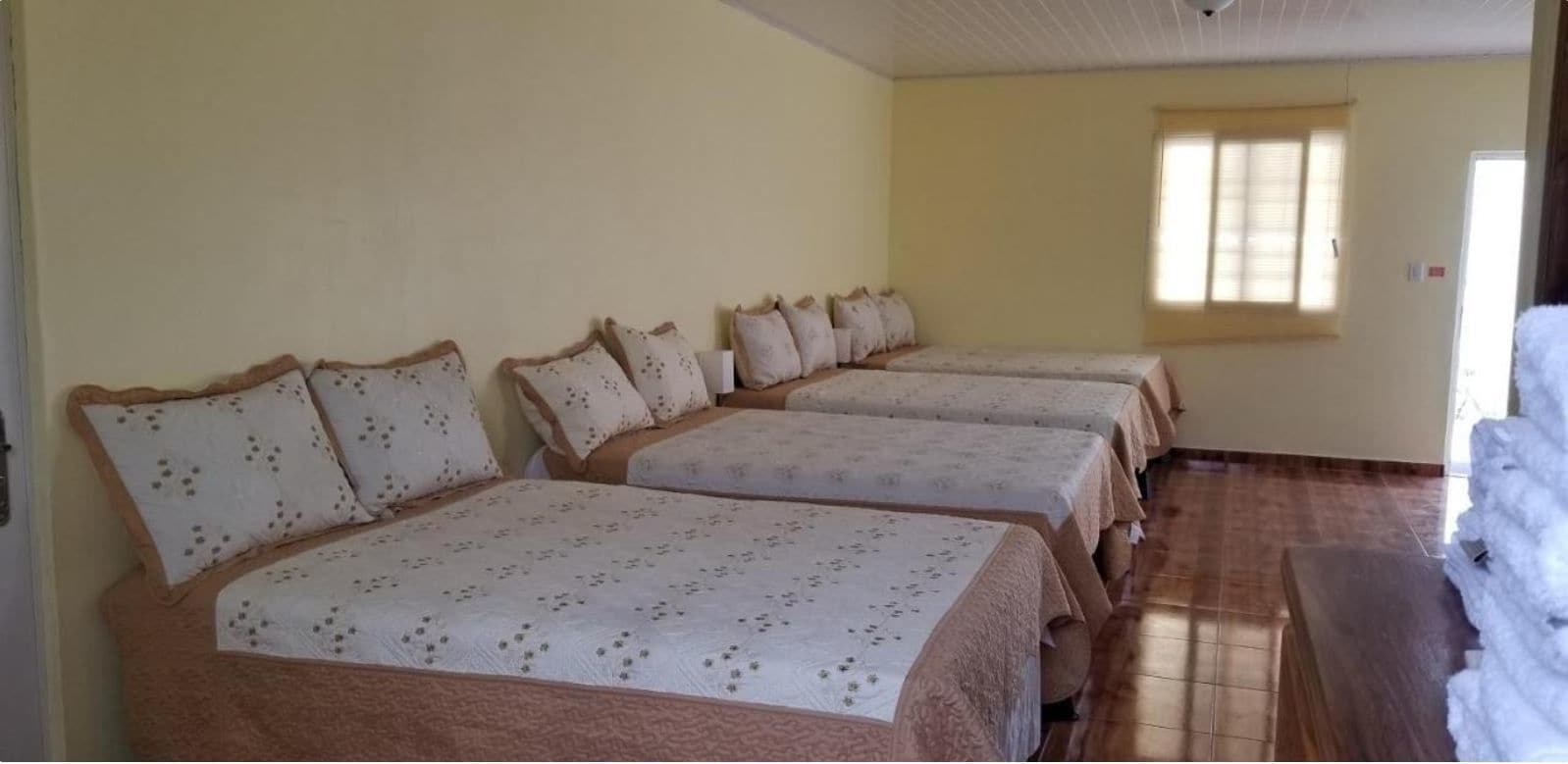 A room with four beds aligned against the wall, each with a patterned bedspread and matching pillows.