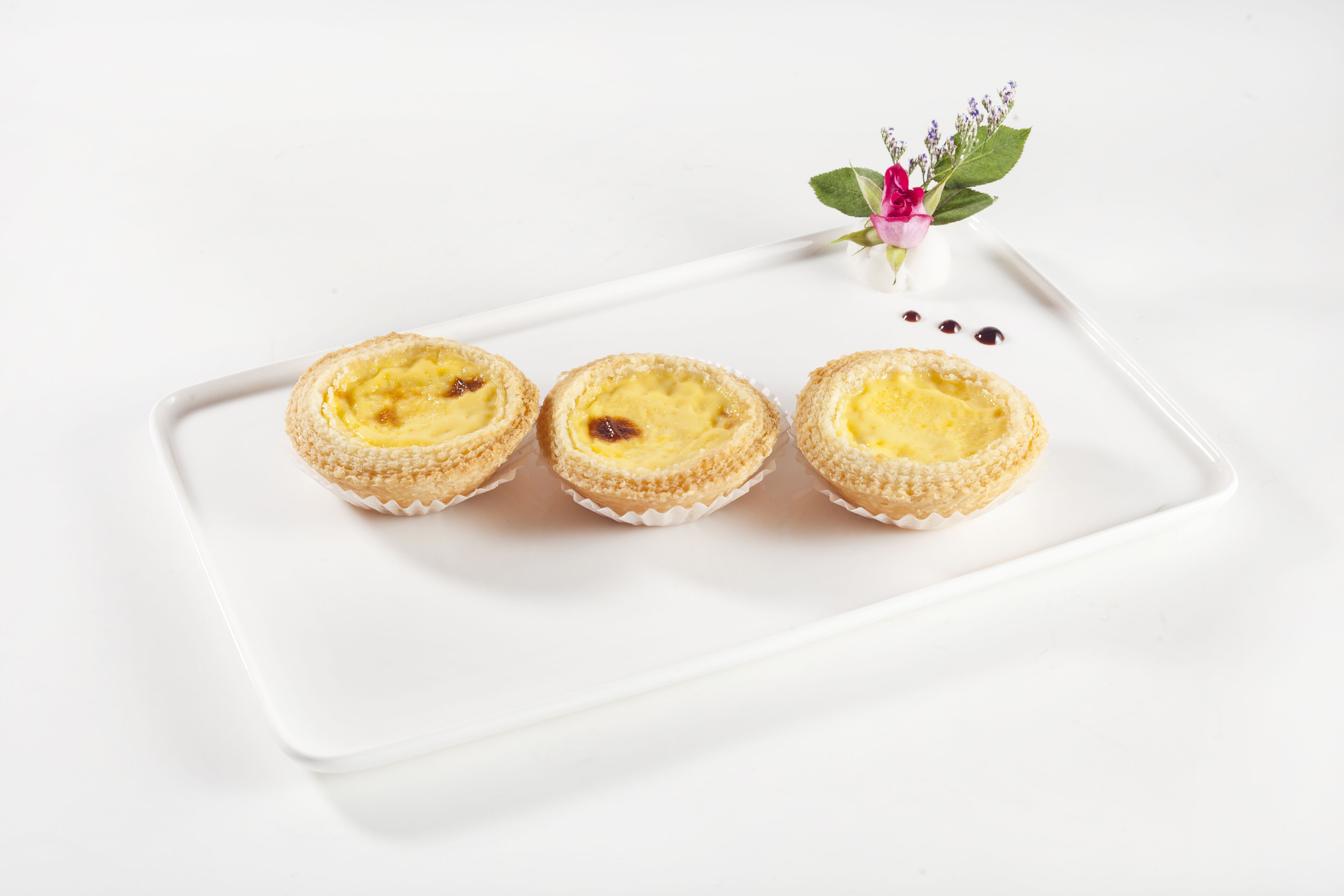 Three custard tarts on a white rectangular plate.