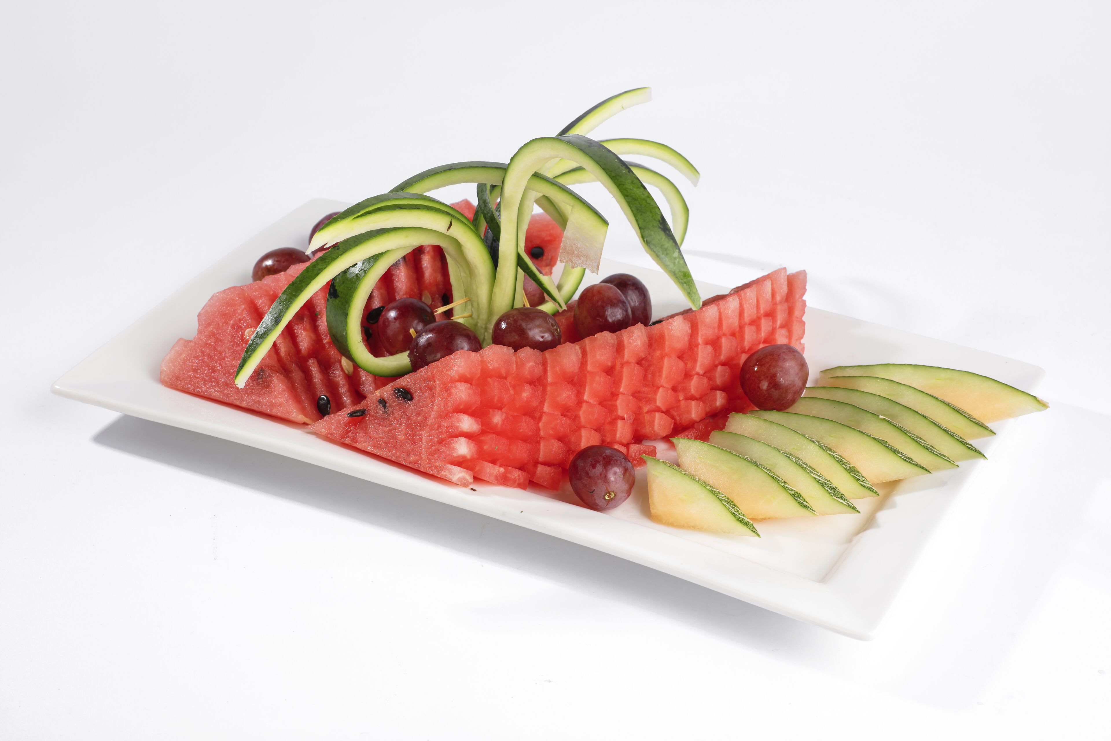 Ein weißer Teller mit Wassermelone, Trauben und Gurkenscheiben.