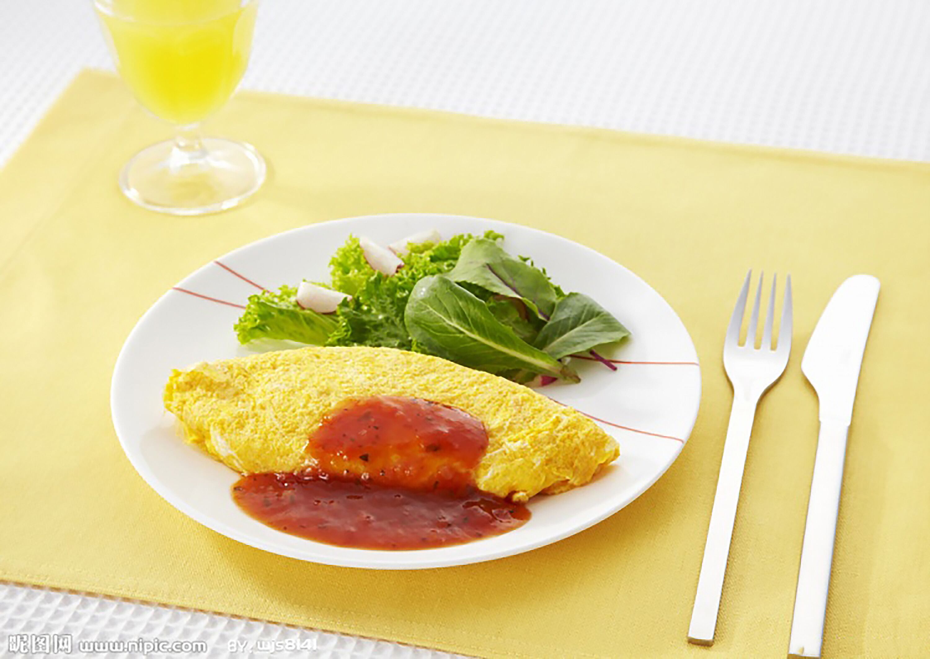 A plate with an omelette, salad, and a glass of juice on a yellow tablecloth.