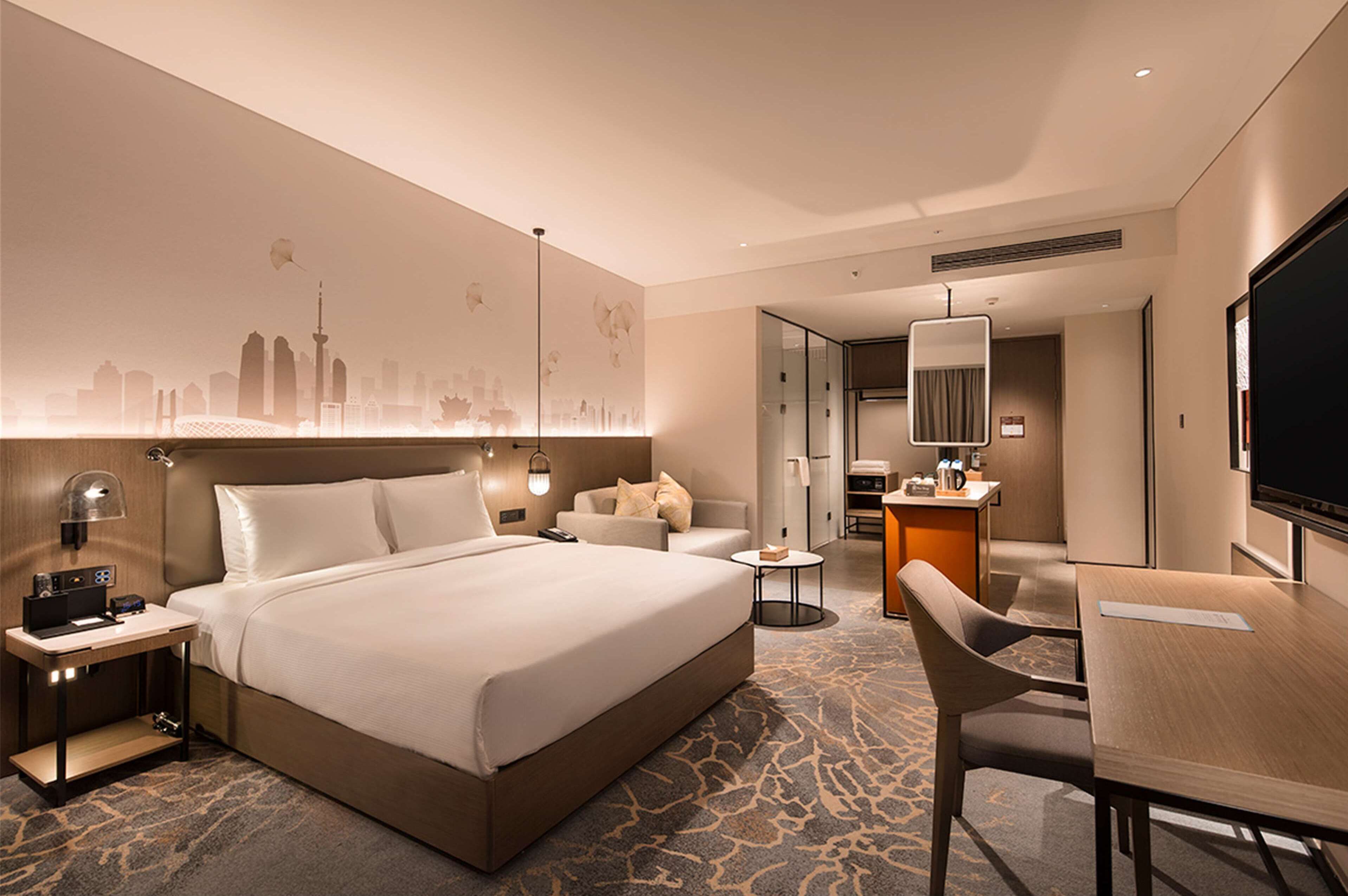 A modern hotel room with a large bed, a desk, a chair, a small table, and a TV.