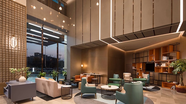 Un vestíbulo amplio con diseño moderno, que incluye un área de descanso con sofás y sillones, una mesa de centro y un ventanal con vistas a la ciudad.
