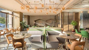 Un interior de restaurante moderno con mesas redondas, asientos acolchados, lámparas colgantes y una zona de cocina visible al fondo.