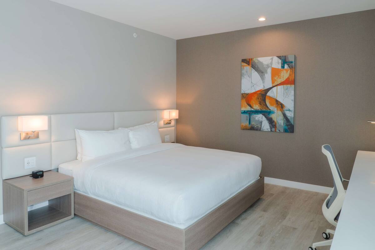 Habitación de hotel moderna con una cama grande, lámparas de noche, mesita de noche, escritorio y una silla.
