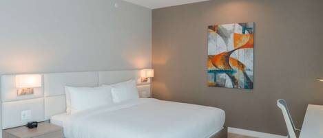 A modern hotel room with a large bed, bedside lamps, a nightstand, a desk, and a chair.
