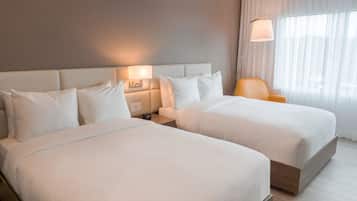 A hotel room with two beds, a nightstand with a lamp, a chair, and a large window with curtains.