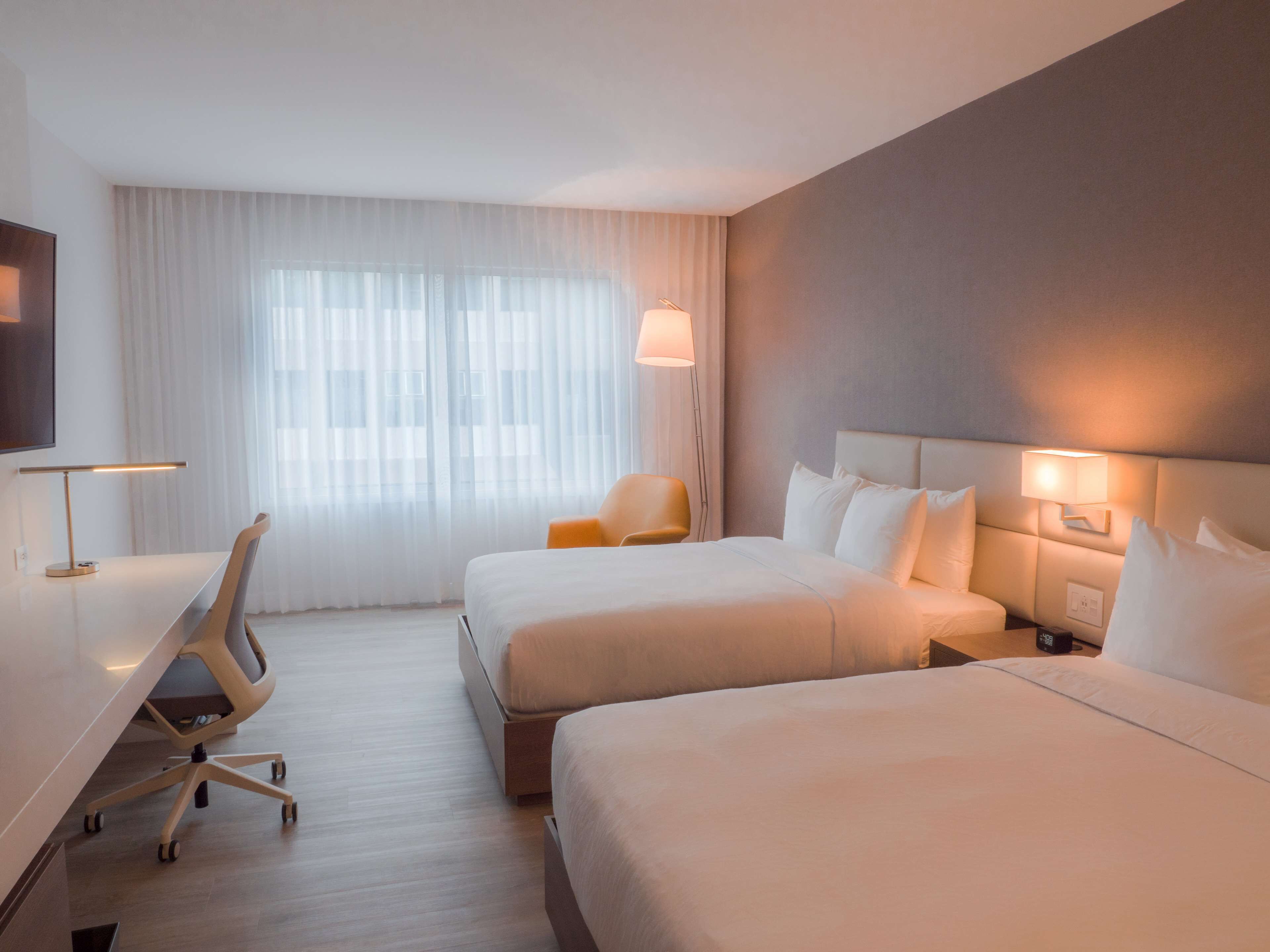 A hotel room with two beds, a desk, a chair, and a TV.