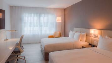 A hotel room with two beds, a desk, a chair, and a TV.