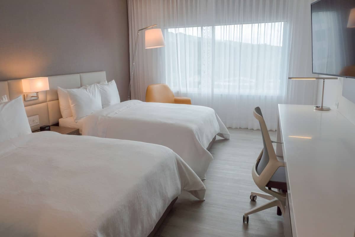 Habitación de hotel con dos camas, un escritorio, una silla y un televisor.