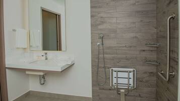 Un baño moderno con pared de ducha de madera, un lavabo blanco con espejo y una barra de apoyo en la ducha.