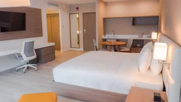 Una habitación de hotel moderna con una cama grande, un escritorio con una silla, una mesita redonda con sillas, un televisor montado en la pared y una mesita de noche con una lámpara.