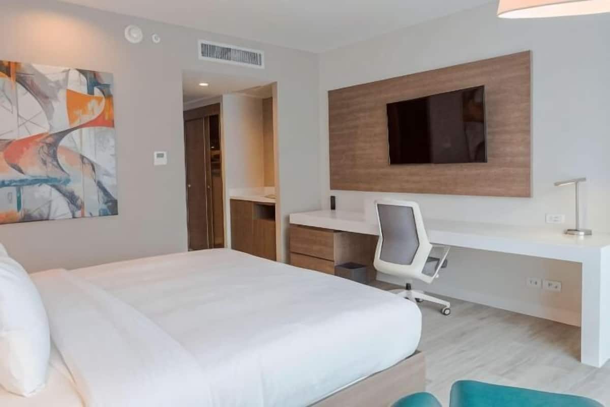 Una habitación de hotel moderna con cama, escritorio, silla, televisión y obras de arte.