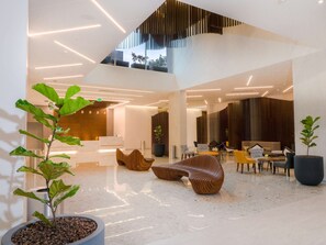 A modern lobby with a high ceiling, geometric light fixtures, and contemporary furniture. - Hilton Garden Inn Santa Ana San Jose (Santa Ana)