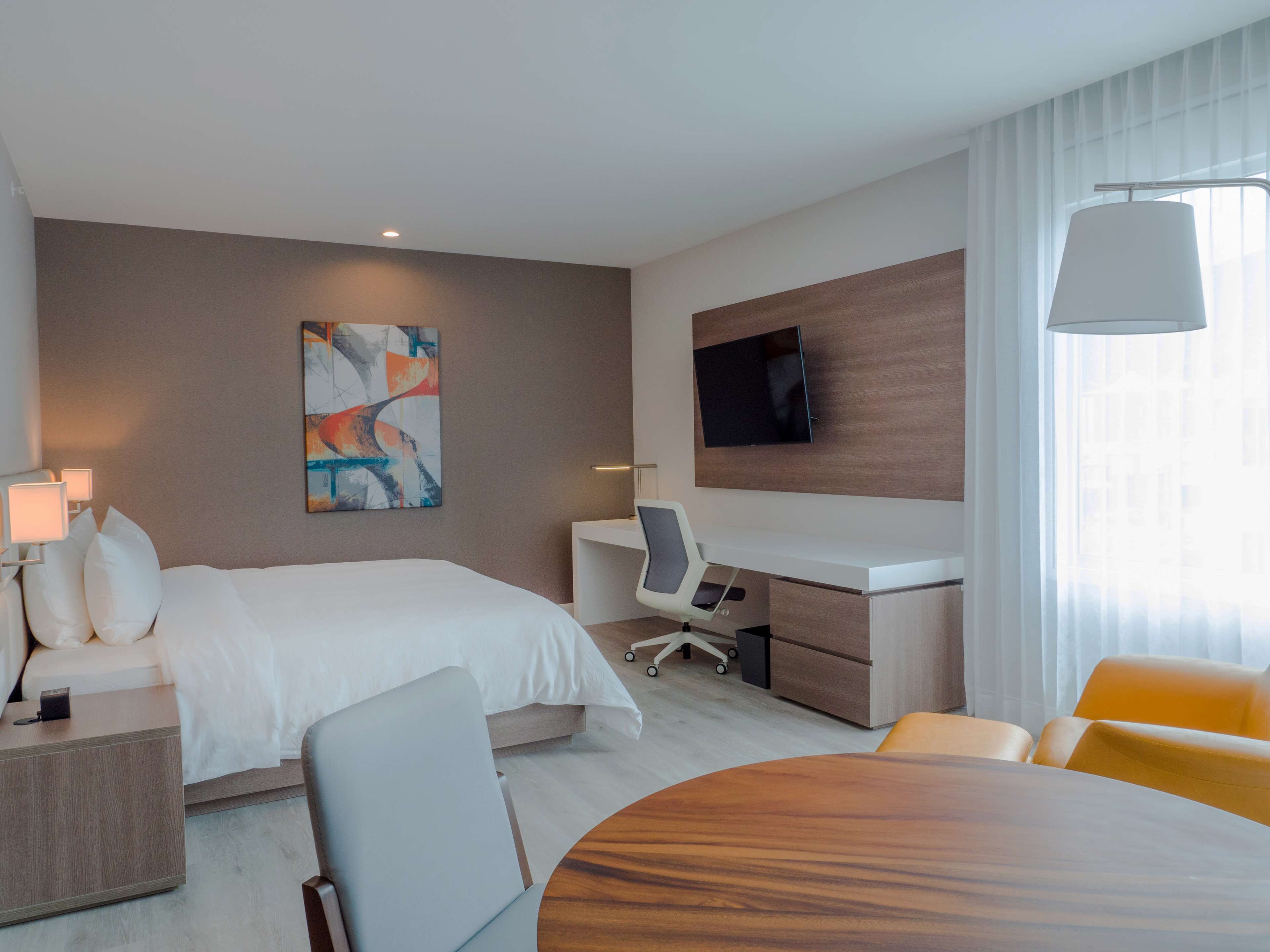 A hotel room with a bed, desk, chair, TV, and a dining table.