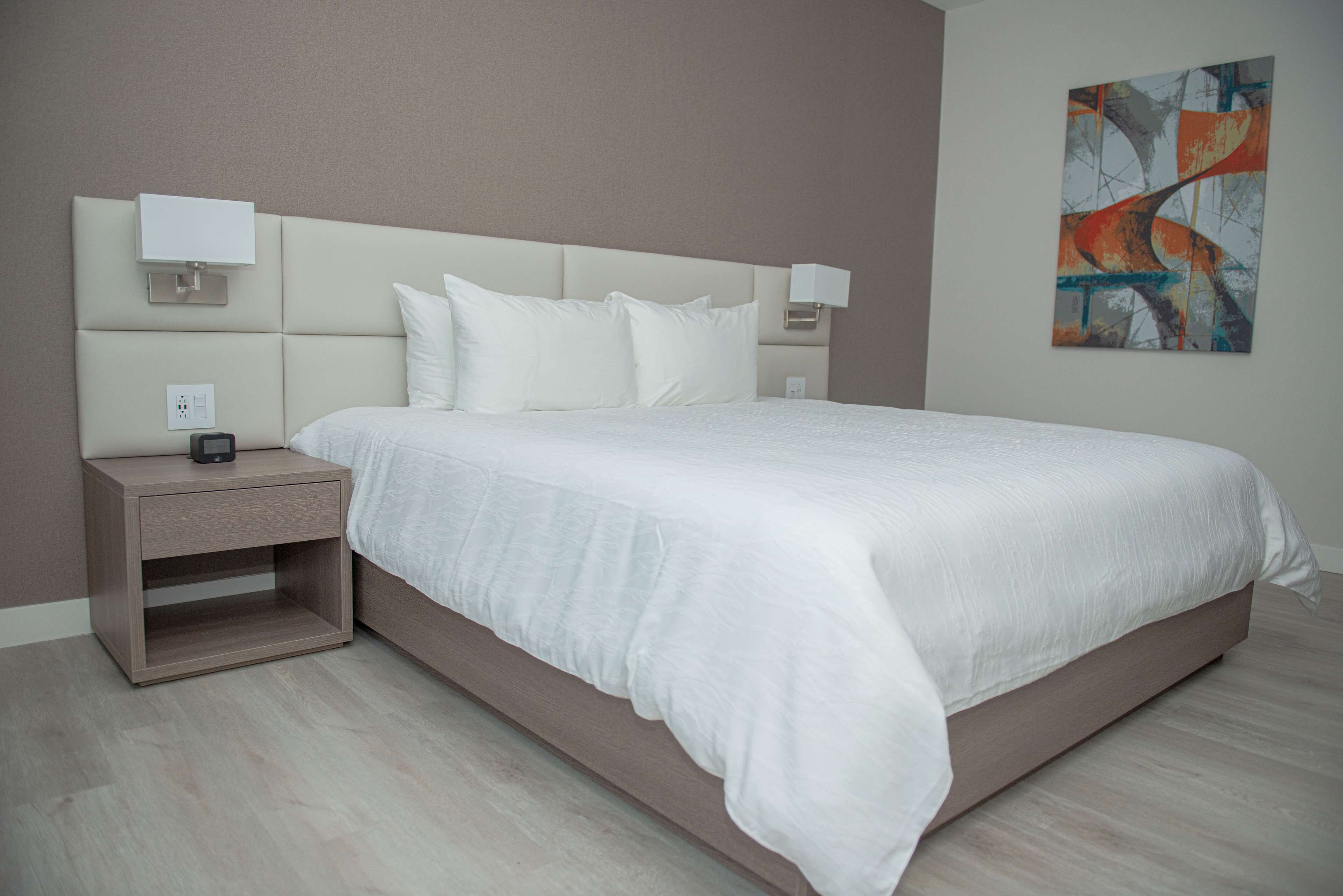 A modern bedroom with a large bed, bedside tables, and a wall-mounted artwork.