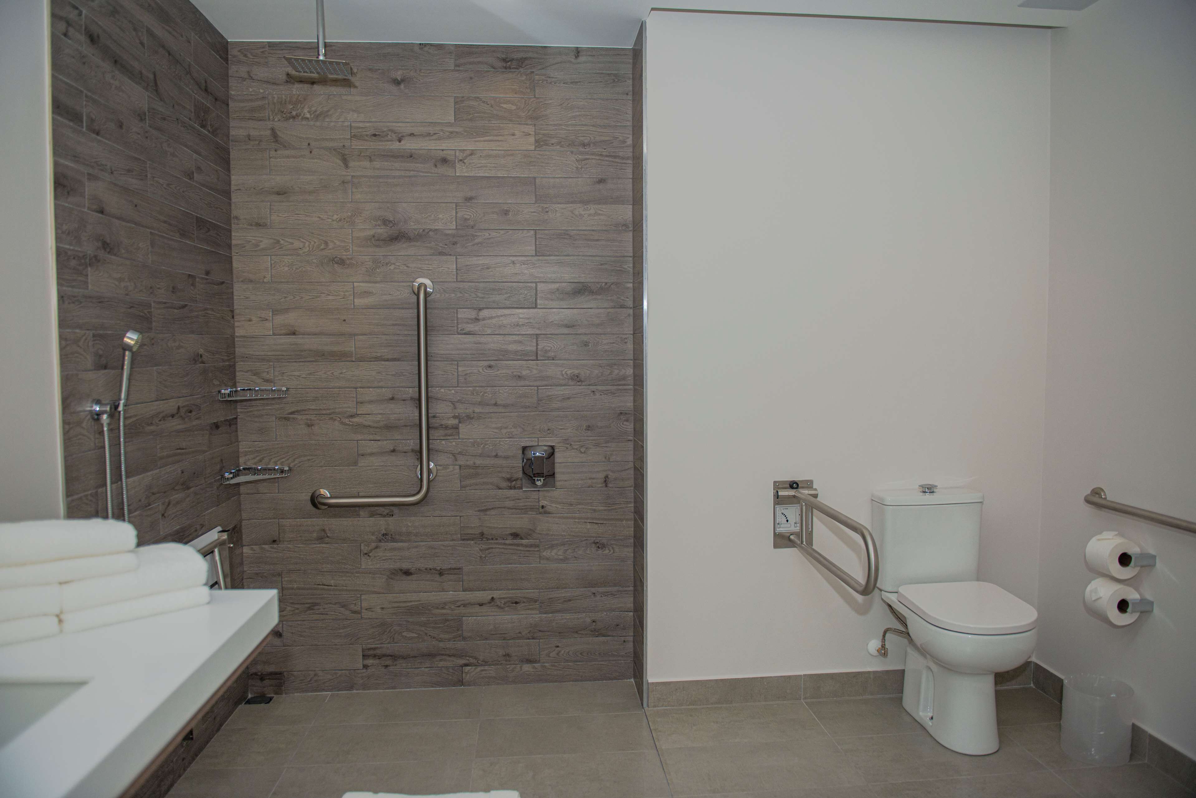 A modern bathroom with a wooden wall, a white sink, a toilet, and a shower area.