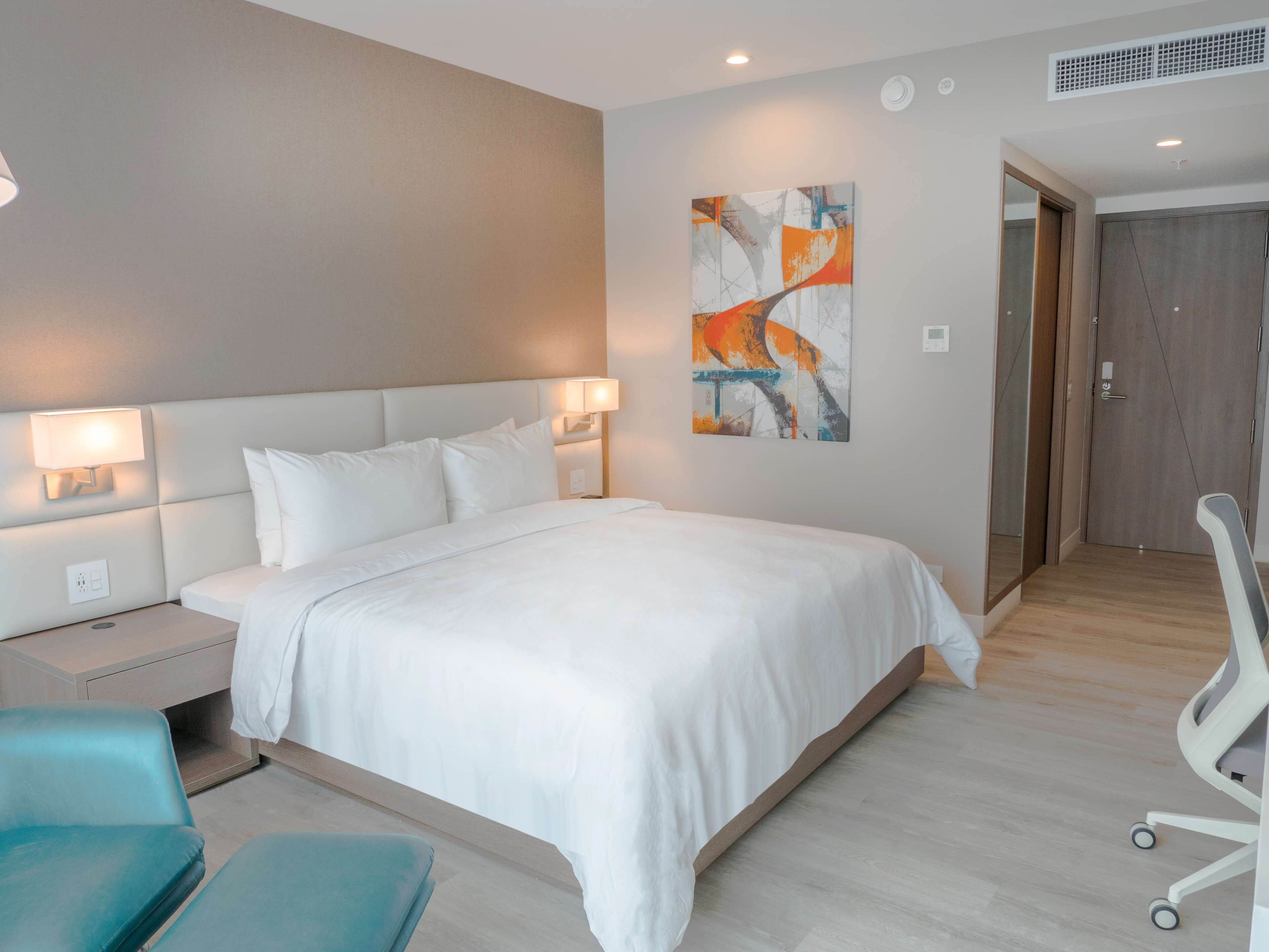 A modern hotel room with a large bed, two bedside lamps, a desk, and a chair.