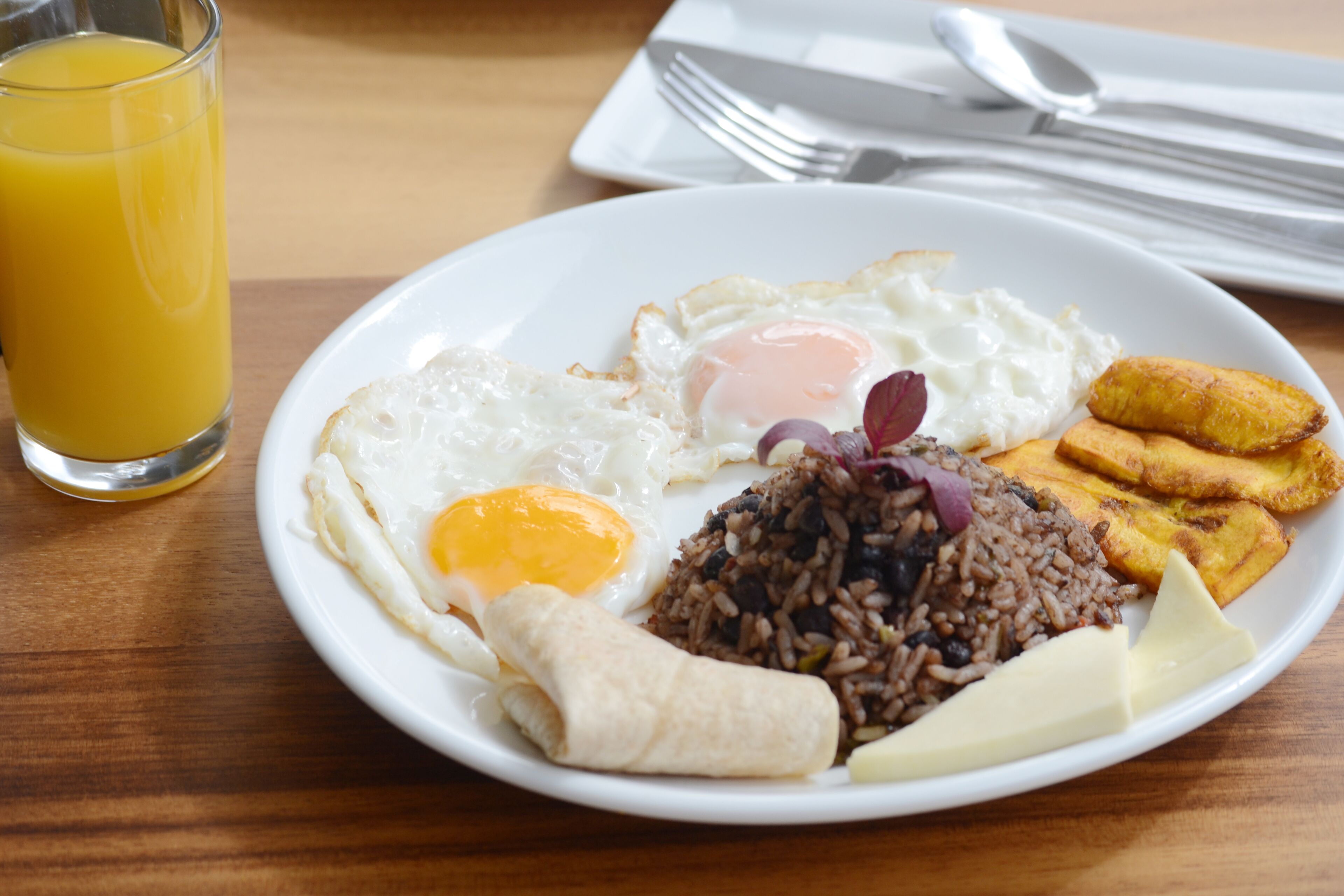 A plate of breakfast food including fried eggs, rice, plantains, and a tortilla.