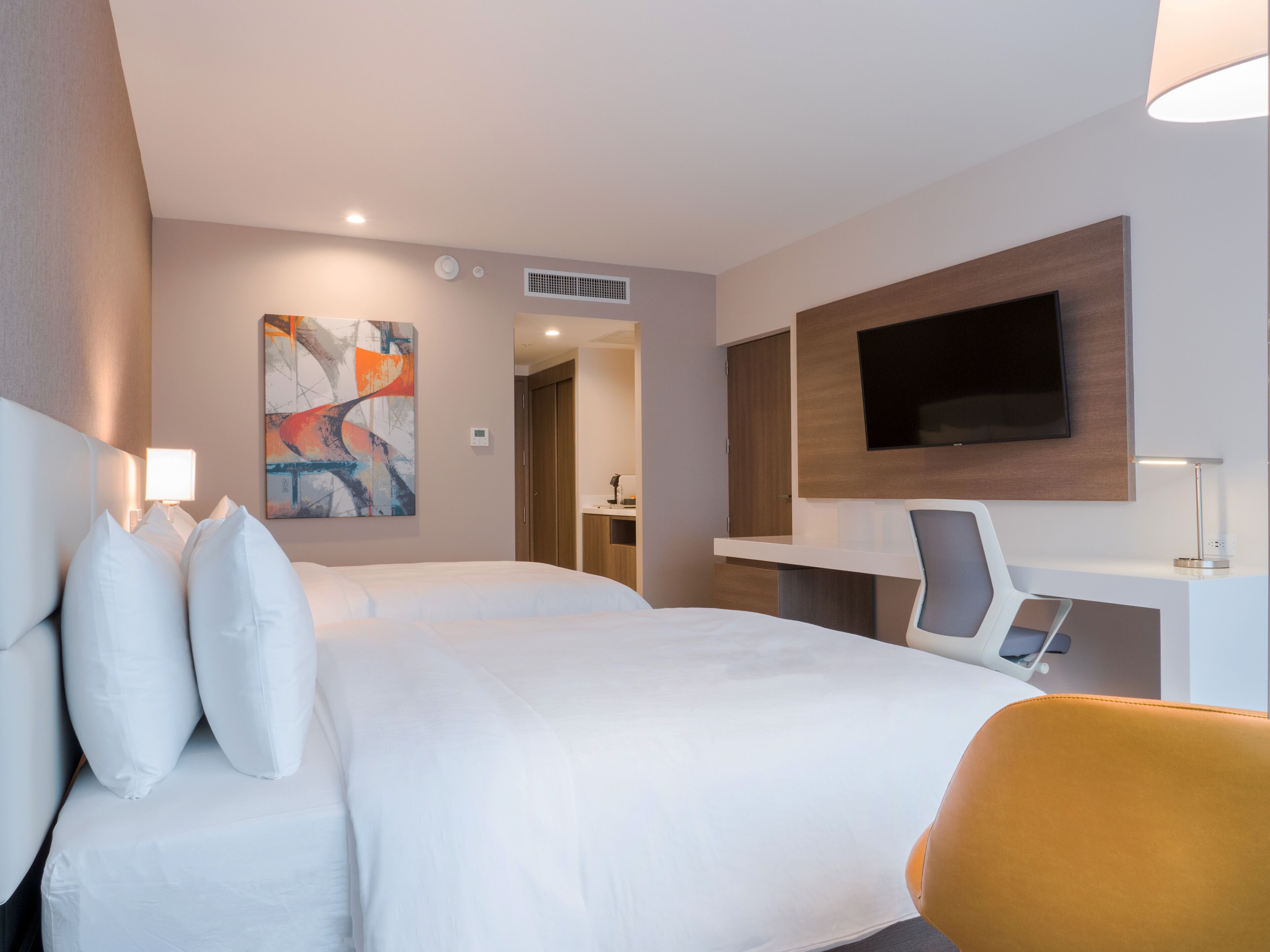 A modern hotel room with a large bed, a desk, a flat-screen TV, and a painting on the wall.