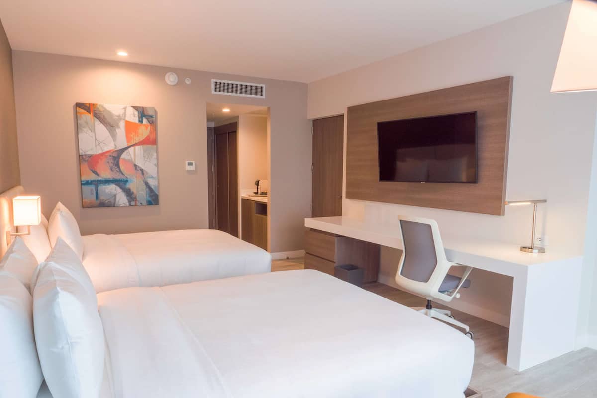 Habitación de hotel con dos camas, un escritorio, una silla, un televisor y obras de arte en la pared.