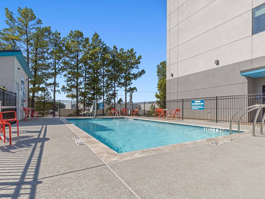 A swimming pool with red chairs and tables, surrounded by a fence and trees.
