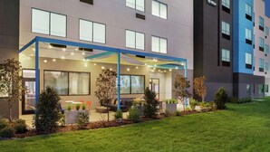A modern hotel with a covered outdoor seating area, a well-maintained lawn, and a clear view of the building's facade.