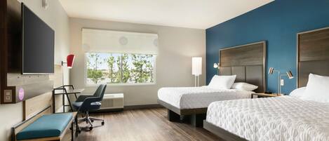 A hotel room with two beds, a desk, a chair, a TV, and a window with a view of trees.