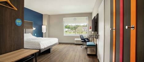 A hotel room with a bed, desk, chair, and a TV on the wall.