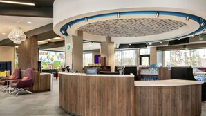 A modern hotel reception area with a curved reception desk, comfortable seating, and a large window offering a view of the city.
