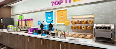 Estación de desayuno con máquinas para hacer gofres, una máquina de café y una variedad de rosquillas.