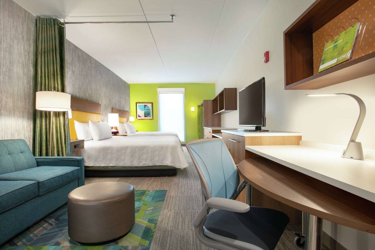 Una habitación de hotel con una cama, un escritorio con ordenador, una silla, un sofá y un televisor.