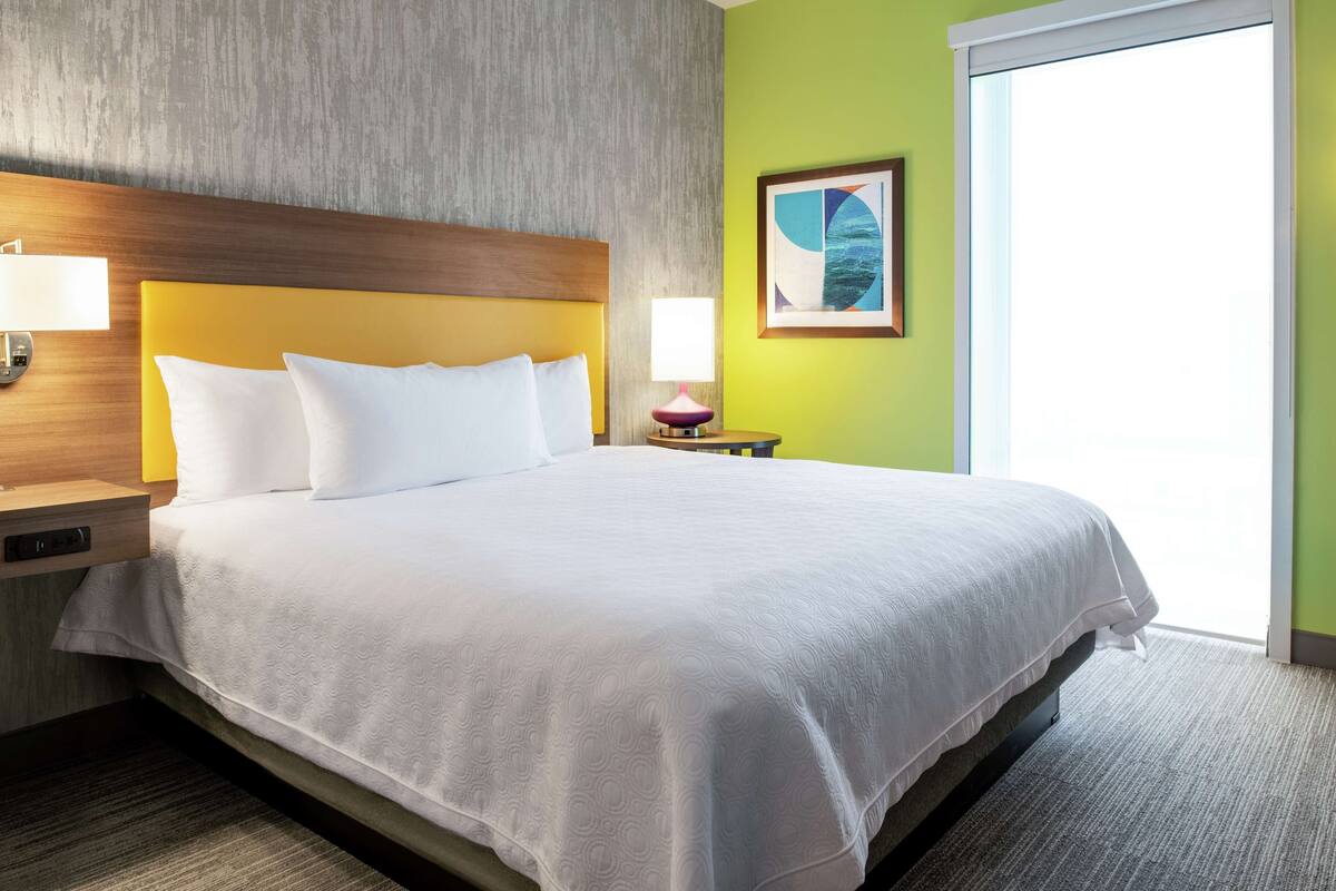 Una habitación de hotel con una cama grande, un cabecero de madera, una mesita de noche con una lámpara y un cuadro en la pared.