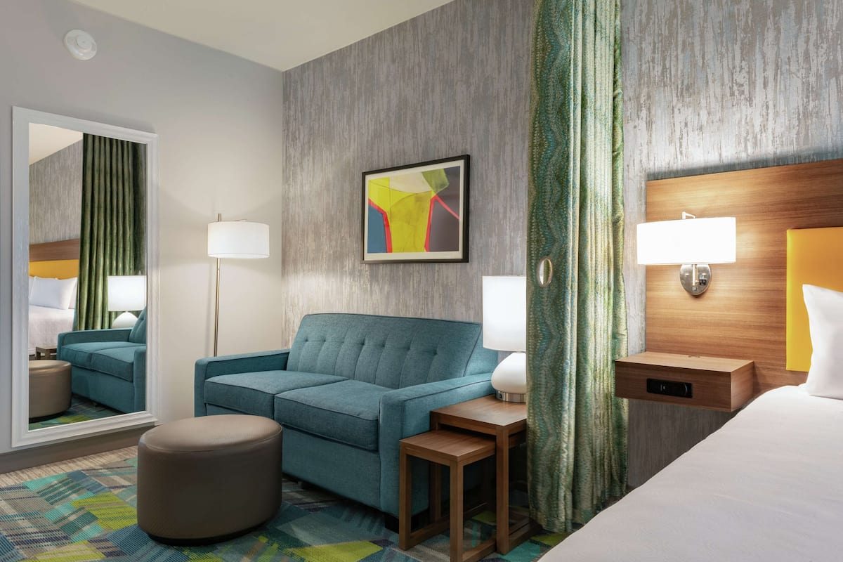 Una habitación de hotel con un sofá color turquesa, una mesita de noche de madera, un espejo y una cama con cabecera.