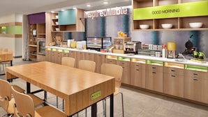Un área de cocina moderna con una mesa y sillas de madera, una barra de desayuno y almacenamiento etiquetado para platos, utensilios y tazones.