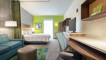 Habitación de hotel con cama, escritorio, silla, sofá, lámpara y televisor.