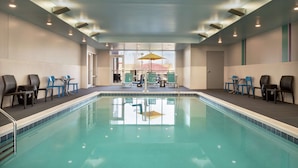 Piscina con sillas y mesas, puerta de vidrio de entrada e iluminación empotrada en el techo.