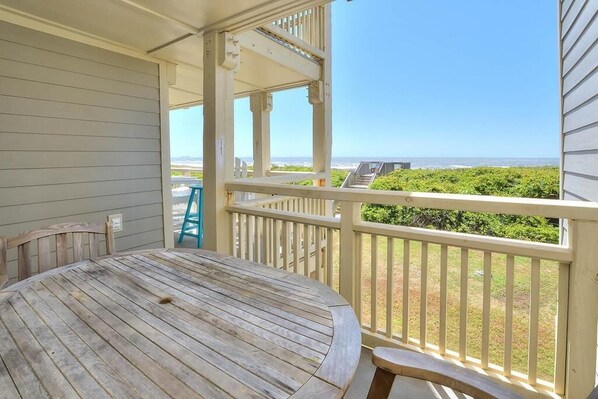 A wooden table and chairs on a balcony with a view of the ocean and greenery.