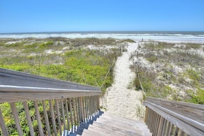 A wooden staircase leading to a beach with sand and sparse vegetation.