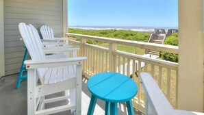 Ein Balkon mit weißen Adirondack-Stühlen und einem türkisblauen Tisch mit Blick auf Strand und Meer.