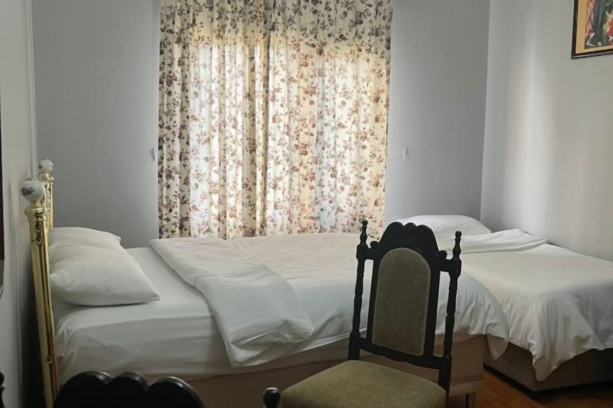 Un dormitorio con dos camas individuales, una silla y una ventana con cortinas florales.