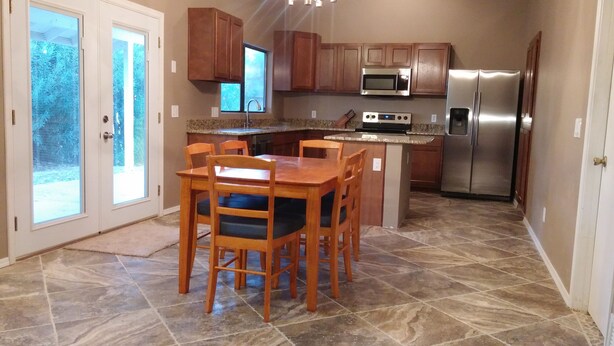 A kitchen with wooden cabinets, a stainless steel refrigerator, a microwave, and a dining area with a table and chairs. - Quiet neighborhood of La Canada (Tucson)