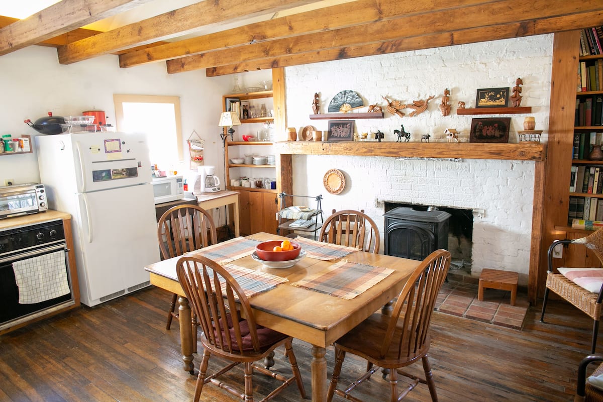 A rustic kitchen with wooden beams, a white brick fireplace, and a dining table with chairs.