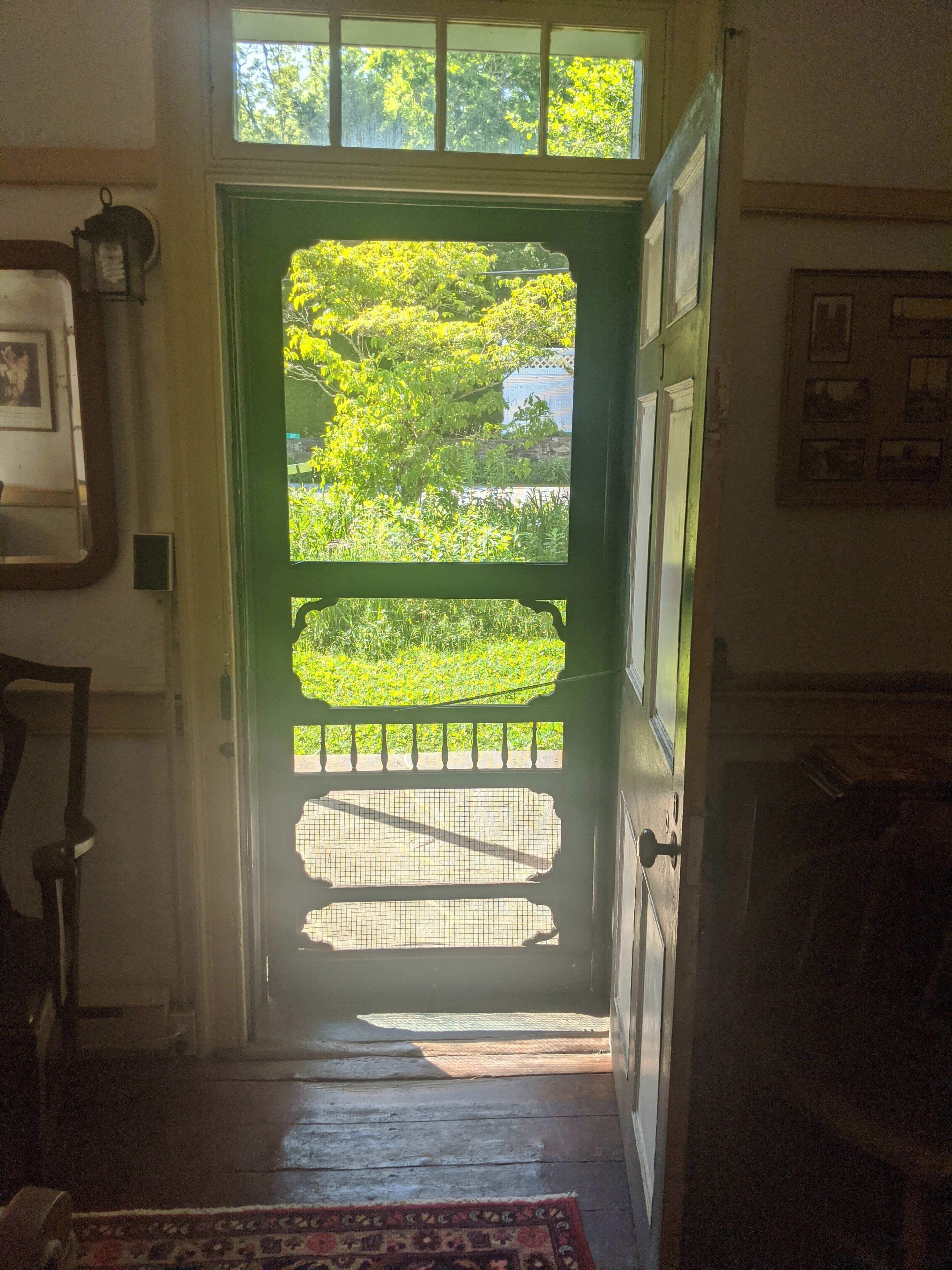 A doorway leading to a balcony with a view of greenery and a building in the background.