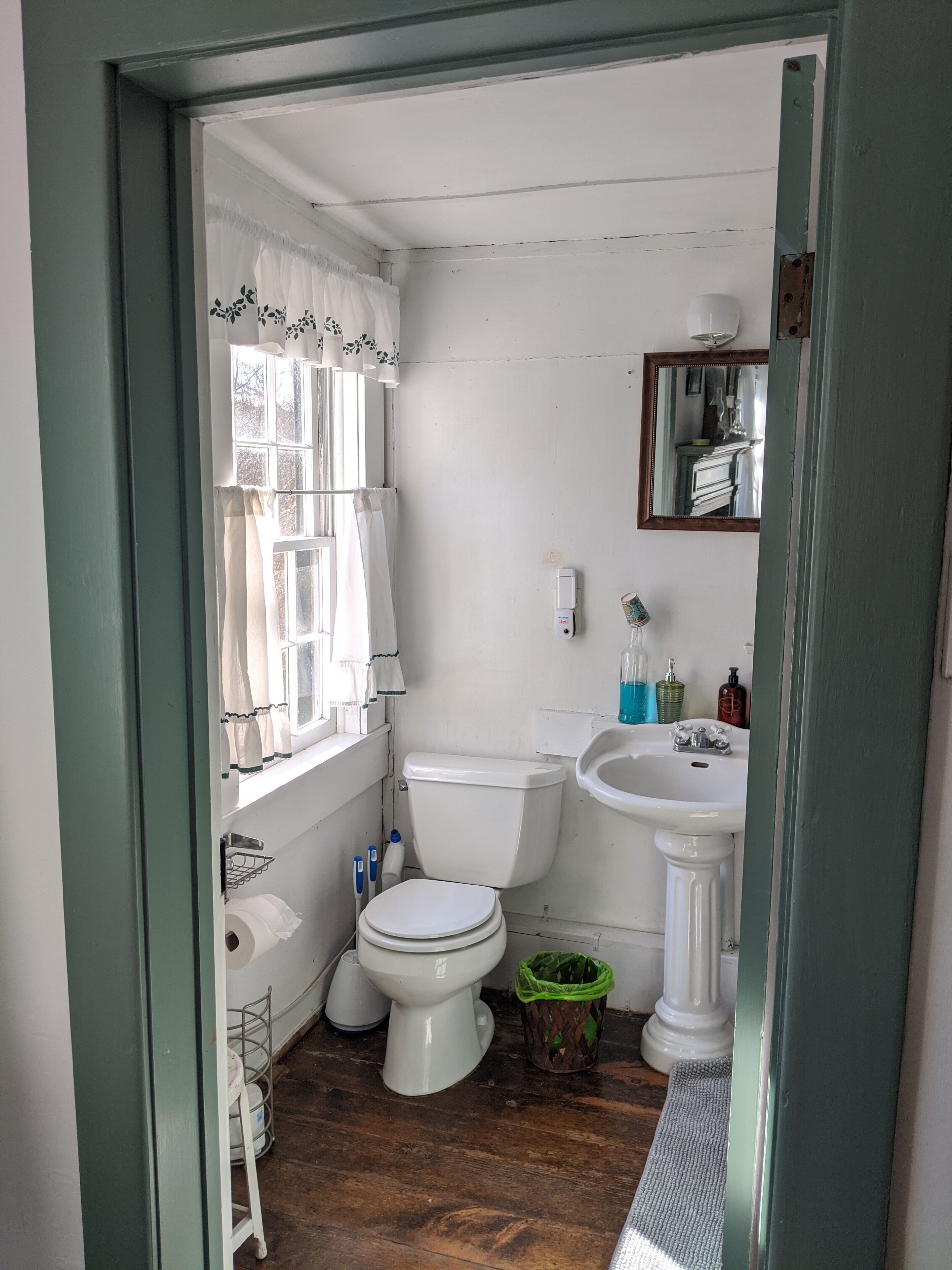 Et lille, rent badeværelse med toilet, håndvask og et vindue med gardiner.