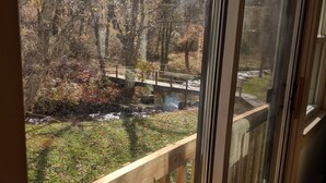 A view from a room with a wooden railing, overlooking a bridge, trees, and a small stream. - The Anderson Cottage Bed & Breakfast (Warm Springs)