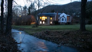 A cabin with a front porch, a small deck, and a stream in front. - The Anderson Cottage Bed & Breakfast (Warm Springs)