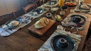 A dining table set with plates, bowls, and a bread basket, indicating a meal is being prepared or served. - The Anderson Cottage Bed & Breakfast (Warm Springs)